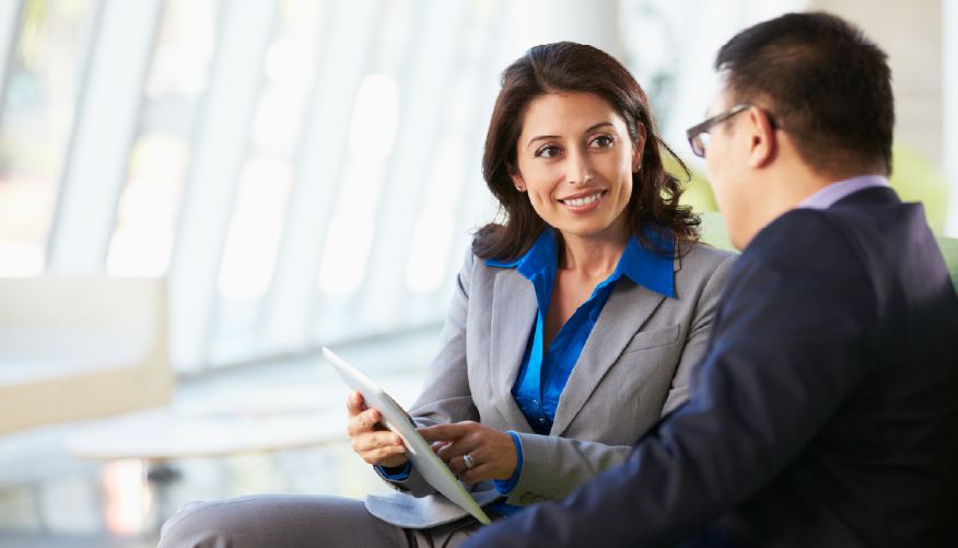 A professional woman and man sit down for a meeting. 