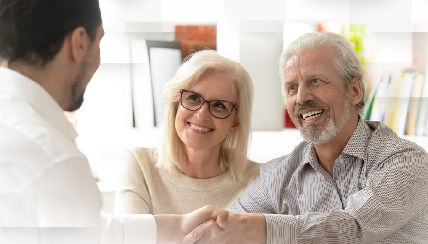 A man and a woman sitting down in a meeting with an insurance advisor, shaking hands.