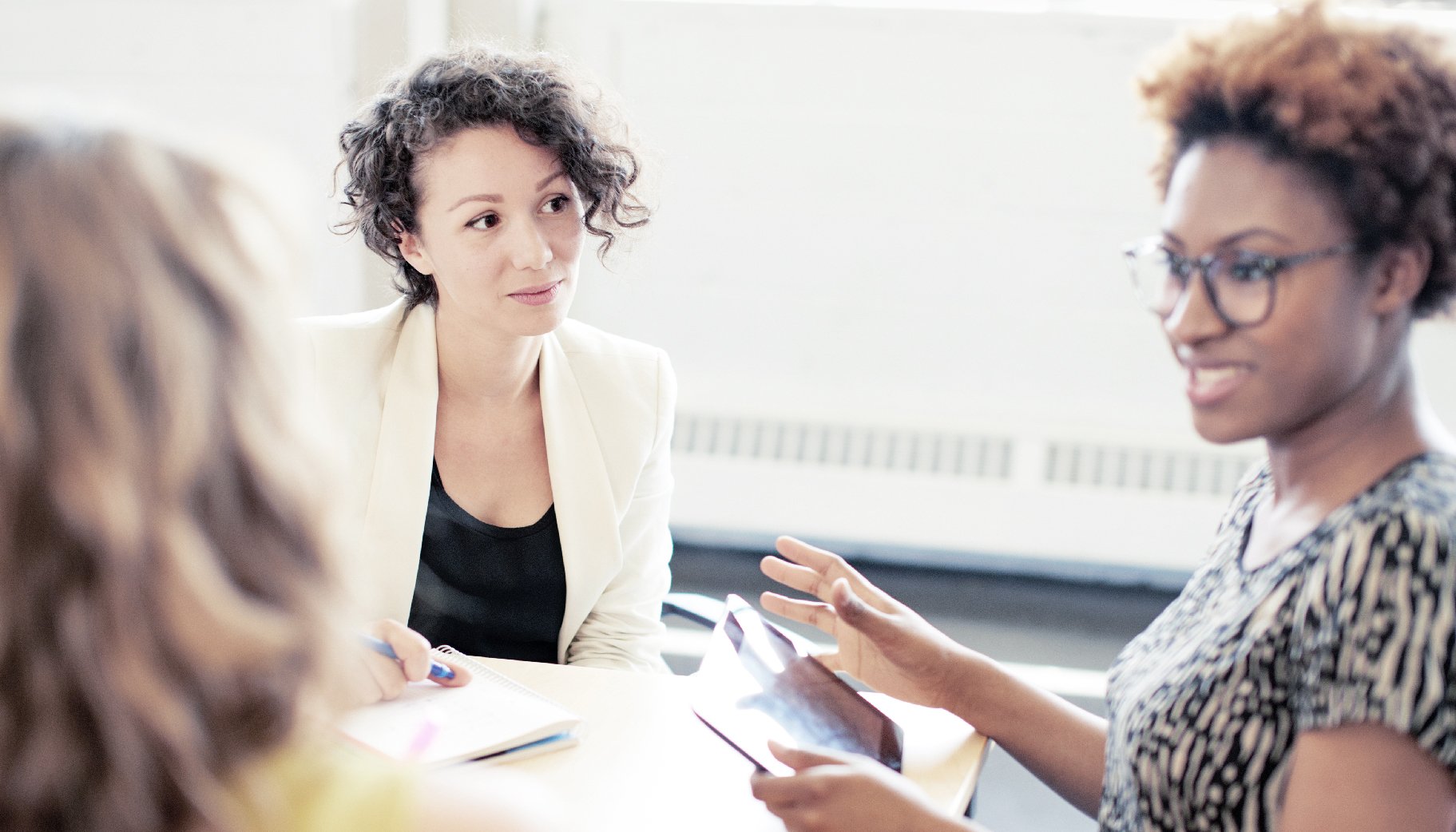 Three people in business attire sitting to have a conversation in an office setting.